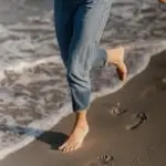 Woman's legs walking barefoot on Timmendorfer Strand beach sand with ocean waves.